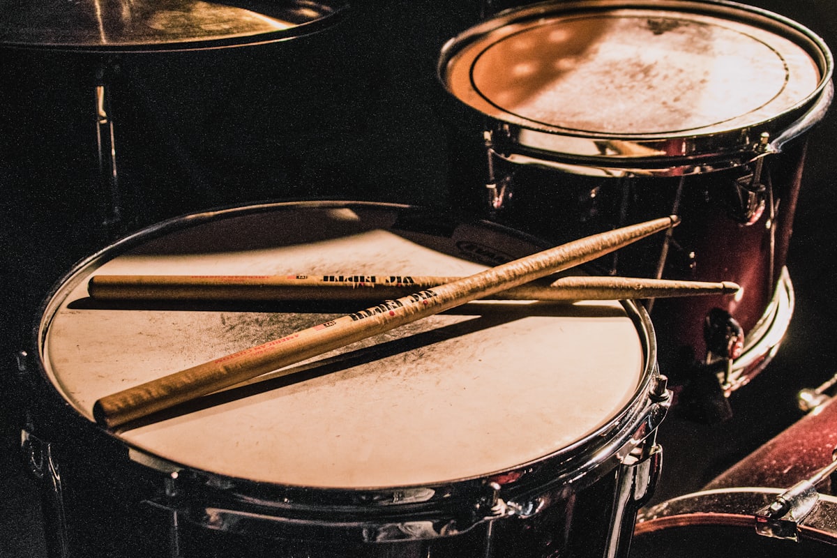 Zwei Drumsticks liegen auf einer Snare Drum im warmen Licht des Übungsraums